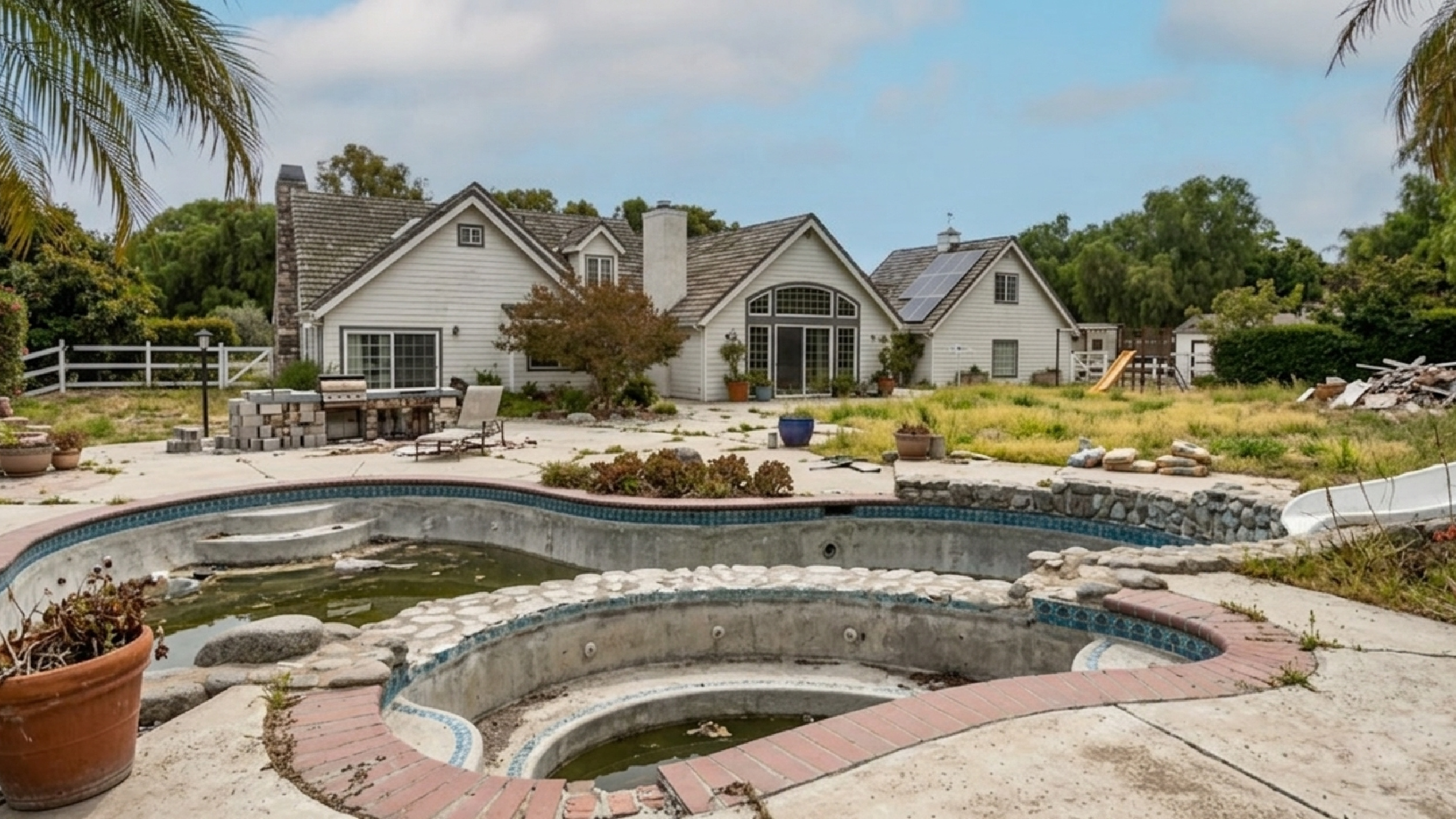 Before — neglected backyard with empty pool and overgrown hardscape in need of renovation